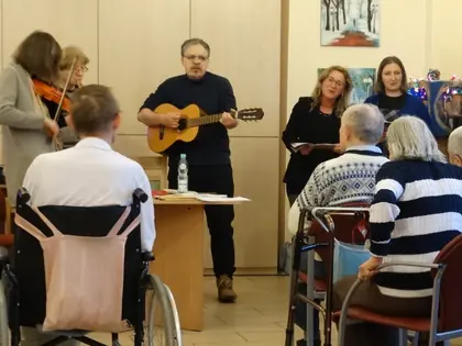 Muzycy z gitarą i skrzypcami kolędują dla mieszkańców w świetlicy