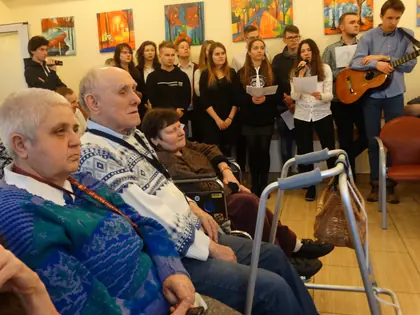 Licealiści śpiewają kolędy z gitarą przed mieszkańcami w świetlicy