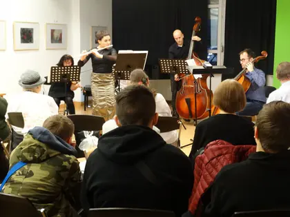 Zespół gra koncert, na pierwszym planie mieszkańcy i młodzież widziani od tyłu