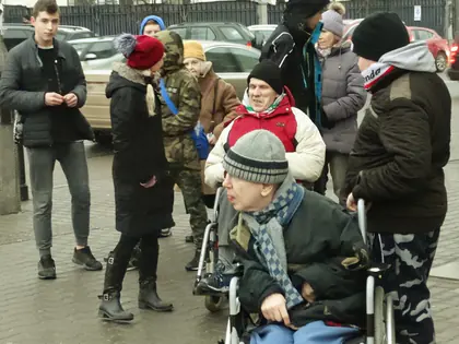 Grupa mieszkańców i młodzieży w czapkach i kurtkach na spacerze po mieście