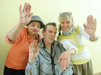 Mieszkanka i mieszkaniec z opiekunką pokazują dłonie z narysowaną prostą linią