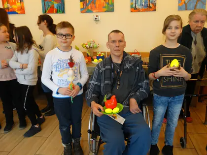 Dzieci i mieszkaniec na wózku pozują z kolorowymi pisankami