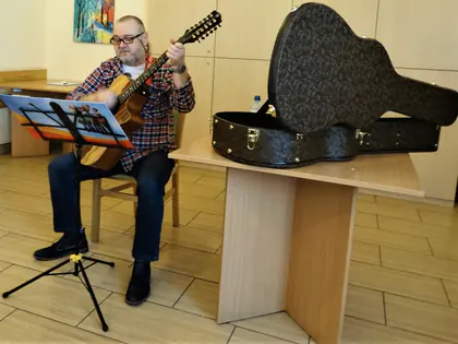 Muzyk gra na gitarze dwunastostrunowej z nut, obok otwarty futerał