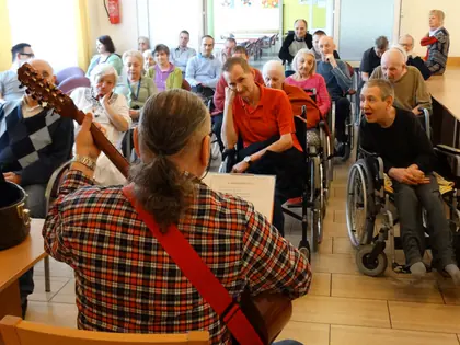Gitarzysta śpiewa z mieszkańcami siedzącymi w świetlicy