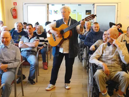 Pieśniarka z gitarą śpiewa wśród mieszkańców w świetlicy
