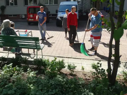 Mieszkańcy i uczniowie zamiatają podwórko przed Domem podczas akcji Eko-Dzień