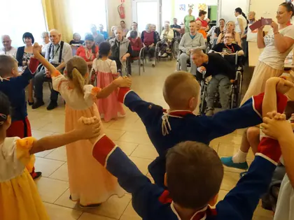 Przedszkolaki w strojach ludowych tańczą w kole przed mieszkańcami
