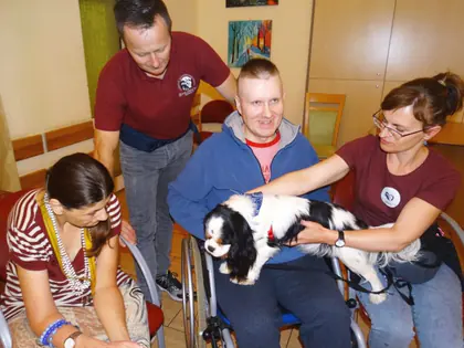 Wolontariusze fundacji Husky Team z psem przy mieszkańcu na wózku