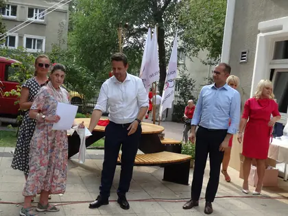 Goście i organizatorzy olimpiady stoją przed budynkiem przy taśmie