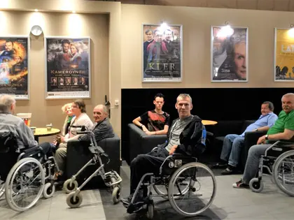 Mieszkańcy na wózkach w holu kina przed plakatami filmowymi