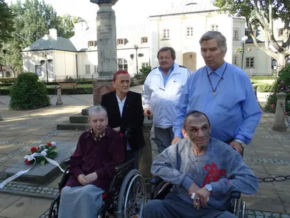 Uczestnicy wycieczki, w tym dwie osoby na wózkach, przy pomniku w parku