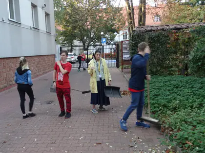 Mieszkańcy i opiekunowie grabią liście przy budynku Domu