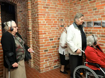 Mieszkańcy ze słuchawkami w ceglanej piwnicy muzeum, jedna kobieta na wózku