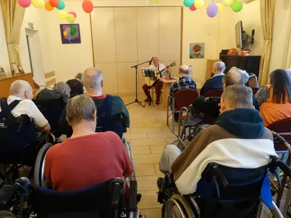 Pieśniarka z gitarą występuje przed mieszkańcami w świetlicy z balonami