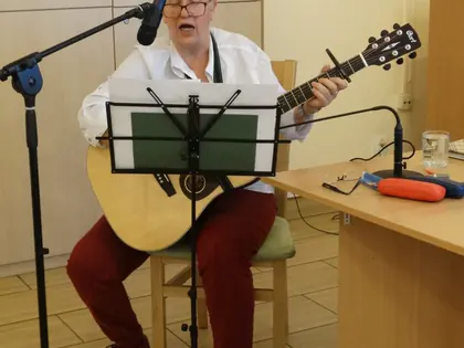 Kobieta w białej koszuli gra na gitarze i śpiewa do mikrofonu