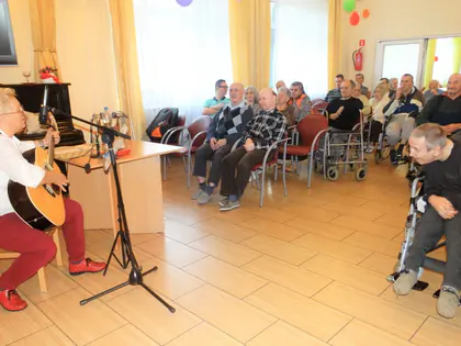 Gitarzystka gra przed mieszkańcami siedzącymi w półkolu w świetlicy