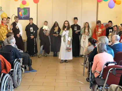 Młodzież w strojach zakonników i świętych stoi przed mieszkańcami