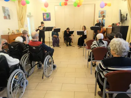 Muzycy grają w głębi świetlicy, na pierwszym planie mieszkańcy na wózkach