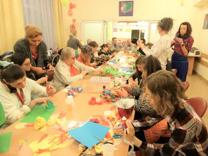 Mieszkańcy i goście przy długim stole sklejają papierowy łańcuch choinkowy