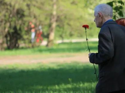 Starszy mężczyzna z czerwonym goździkiem w dłoni idzie przez park