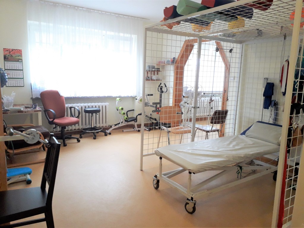 Sala terapii ruchowej z leżanką rehabilitacyjną i sprzętem do usprawniania.