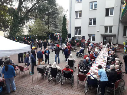 Długie stoły z gośćmi i mieszkańcami na podwórku Domu
