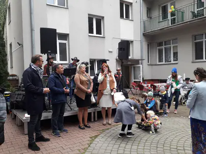 Organizatorzy i goście przemawiają przed sceną na podwórku Domu
