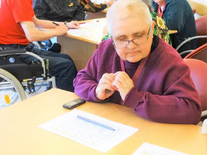 Mieszkanka z kartą do bingo przy stole, w tle inni gracze