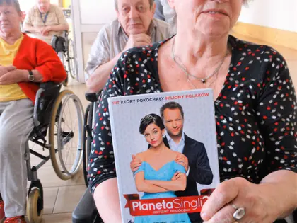 Mieszkanka pokazuje okładkę filmu „Planeta Singli”, w tle mieszkańcy