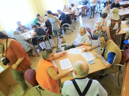 Mieszkańcy i pracownicy przy stołach grają w bingo w świetlicy