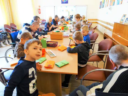 Przedszkolaki i mieszkańcy tworzą kartki przy wspólnym stole