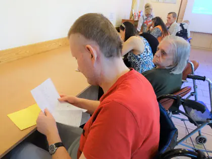 Mieszkaniec czyta odręcznie napisany list przy stole w świetlicy