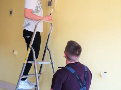 Dwaj młodzi mężczyźni na drabinie malują ścianę na żółto
