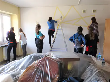 Młodzież okleja ścianę taśmą w geometryczny wzór