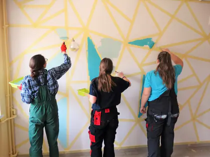 Uczennice malują wałkami geometryczny wzór na ścianie