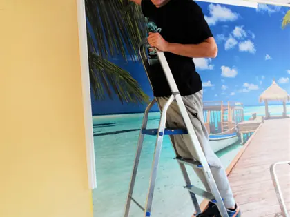 Chłopak na drabinie nakleja fototapetę z plażą