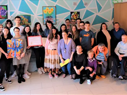 Duża grupa uczniów i mieszkańców pozuje przed ścianą pomalowaną w niebieskie trójkąty