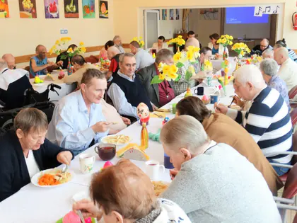Mieszkańcy przy długich stołach z żonkilami podczas wielkanocnego obiadu