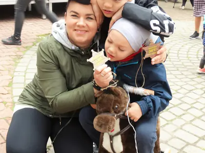 Kobieta przytula dwóch chłopców siedzących na koniku na kółkach