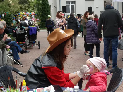 Kobieta w kowbojskim kapeluszu maluje twarz dziewczynce