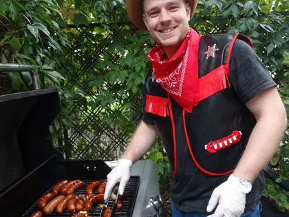 Uśmiechnięty kucharz w kowbojskim kapeluszu grilluje kiełbaski