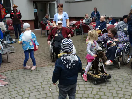 Dzieci bawią się wśród mieszkańców na wózkach siedzących przy stołach