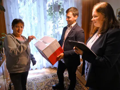 Mieszkanka wrzuca kartę do biało-czerwonej urny trzymanej przez mężczyznę