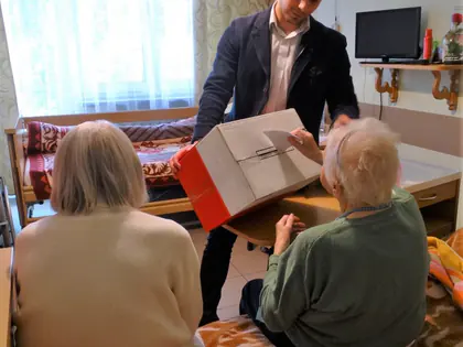Mieszkanka siedząca w fotelu głosuje do przenośnej urny
