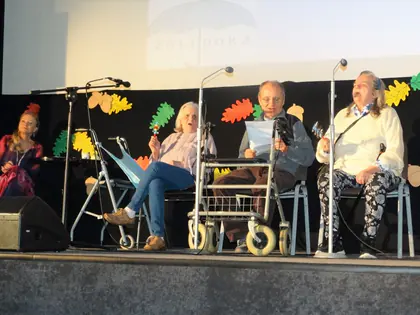Seniorzy śpiewają na scenie festiwalu na tle jesiennych liści
