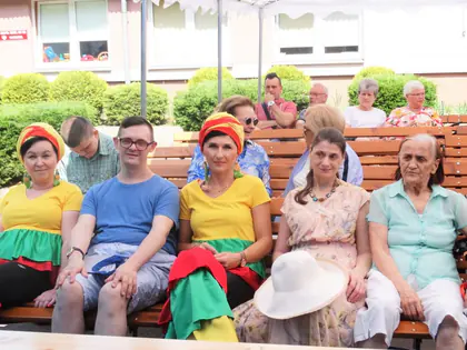 Mieszkańcy i goście w kolorowych chustach siedzą na ławkach podczas pikniku