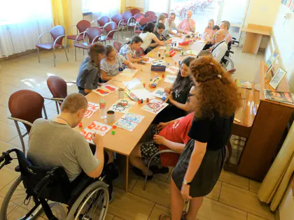 Mieszkańcy i wolontariuszki malują przy długim stole