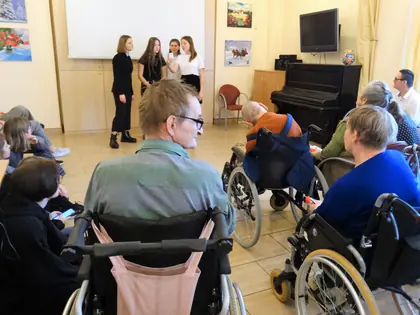Dziewczęta występują przed mieszkańcami siedzącymi na wózkach w świetlicy