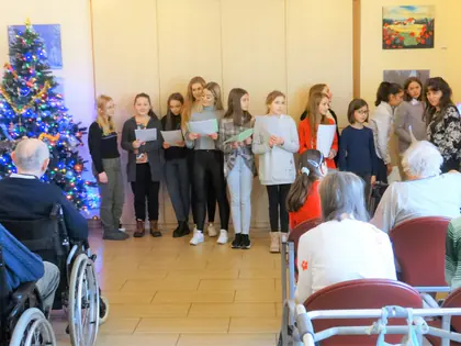 Uczennice śpiewają kolędy przed mieszkańcami w świetlicy obok choinki