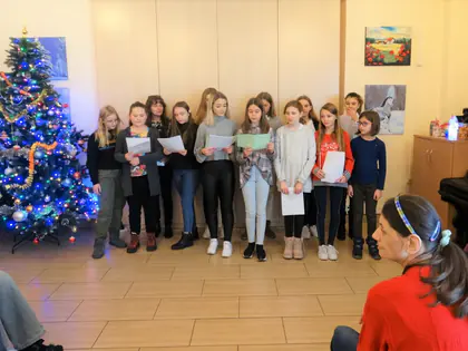 Grupa dziewcząt z kartkami śpiewa przy choince